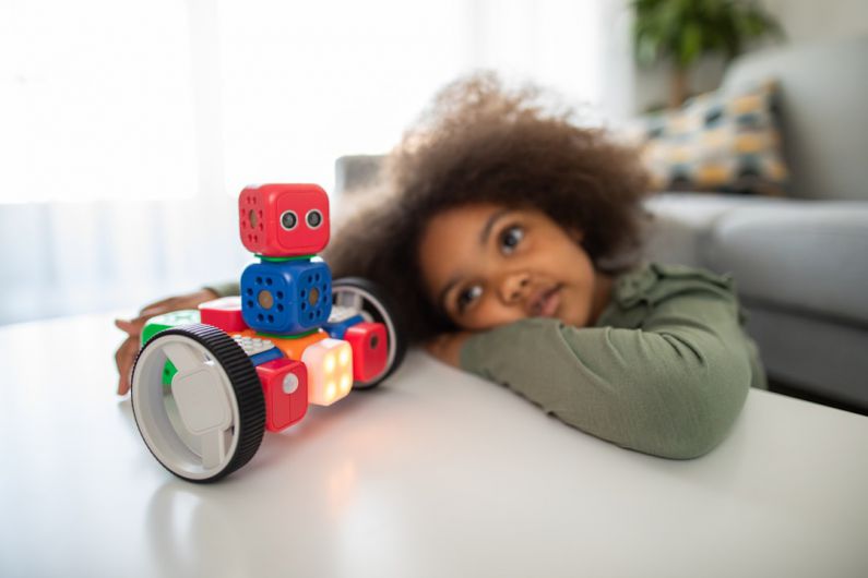 AI Robotics Cost - boy lying on bed playing with red and blue toy truck